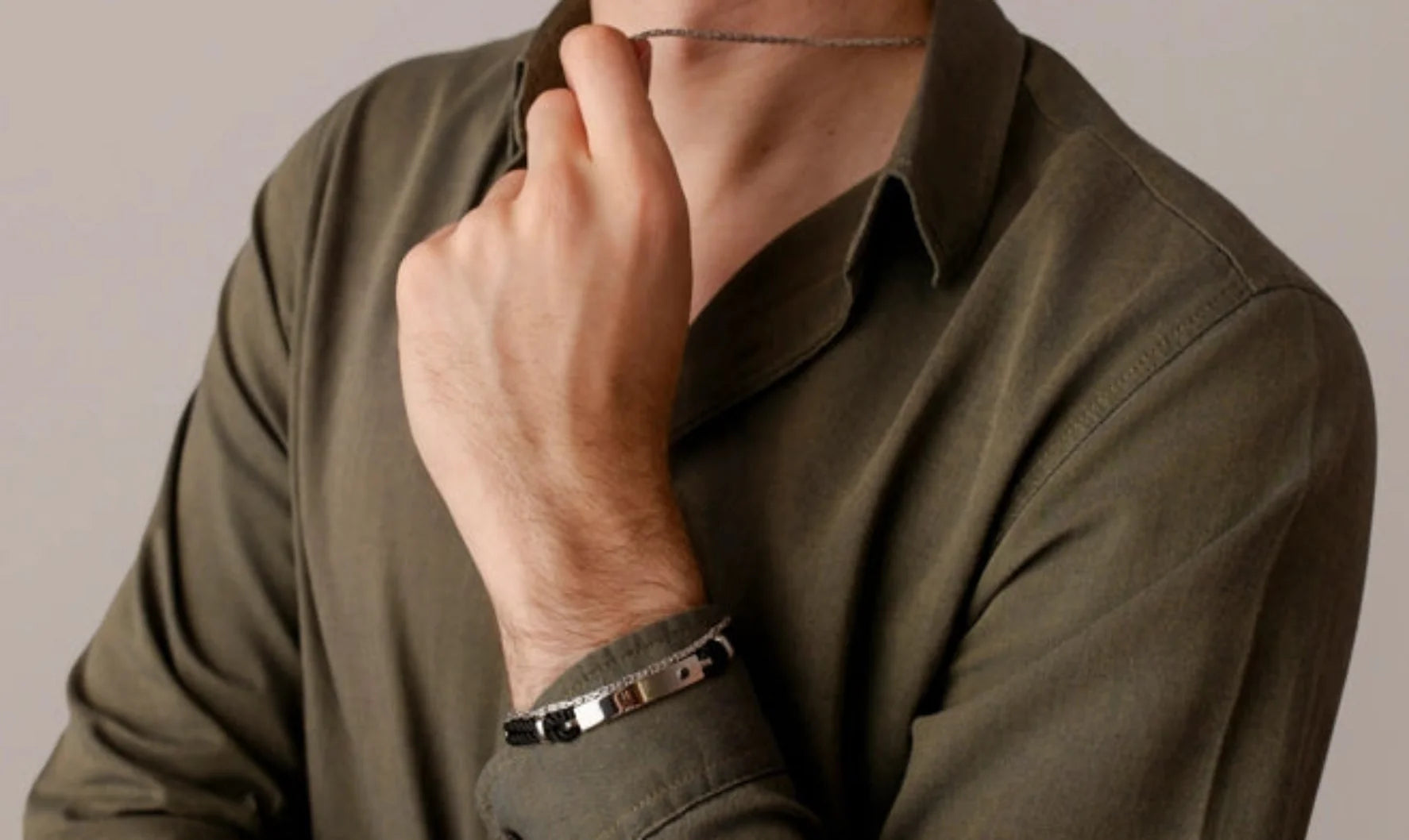 Uomo con camicia verde e gioielli in argento, tra cui bracciale e collana, su sfondo chiaro