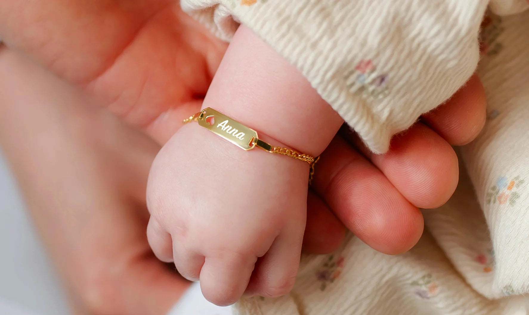 Bracciale neonato in oro con incisione personalizzata al polso di una bambina, gioiello delicato della collezione Nascita Sakrami.