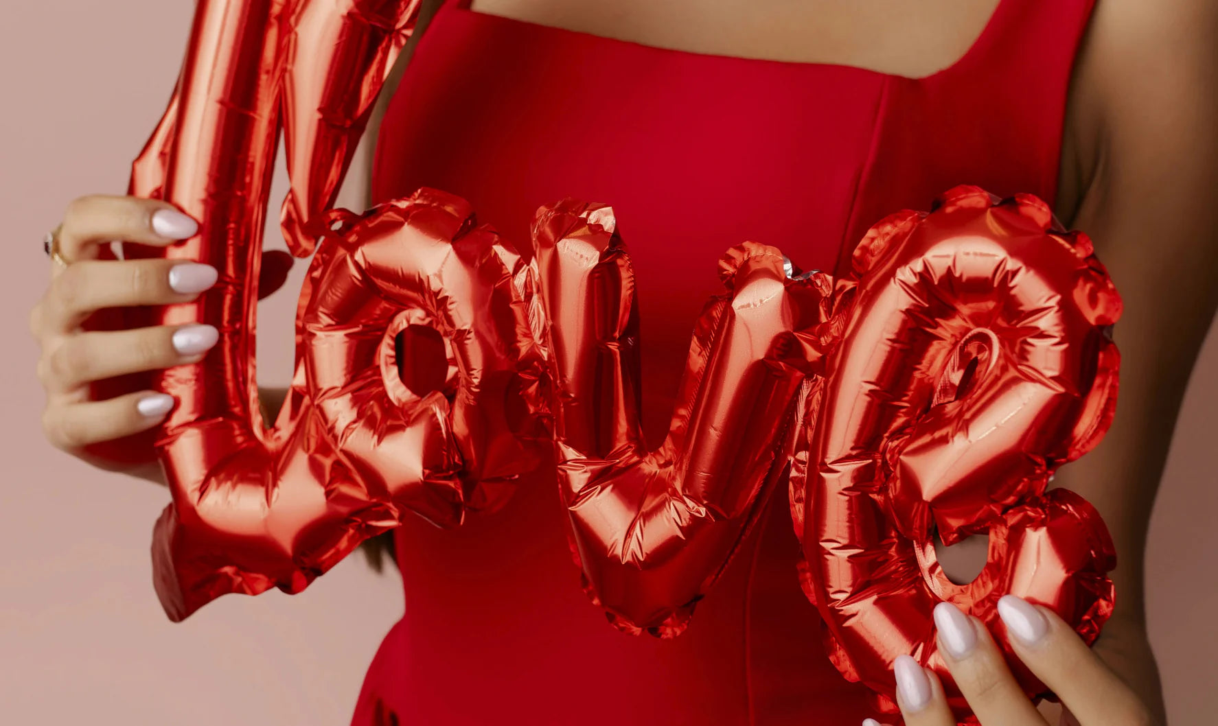 Donna in abito rosso con gioielli Sakrami mentre tiene un palloncino a forma di scritta Love, immagine romantica della collezione San Valentino.